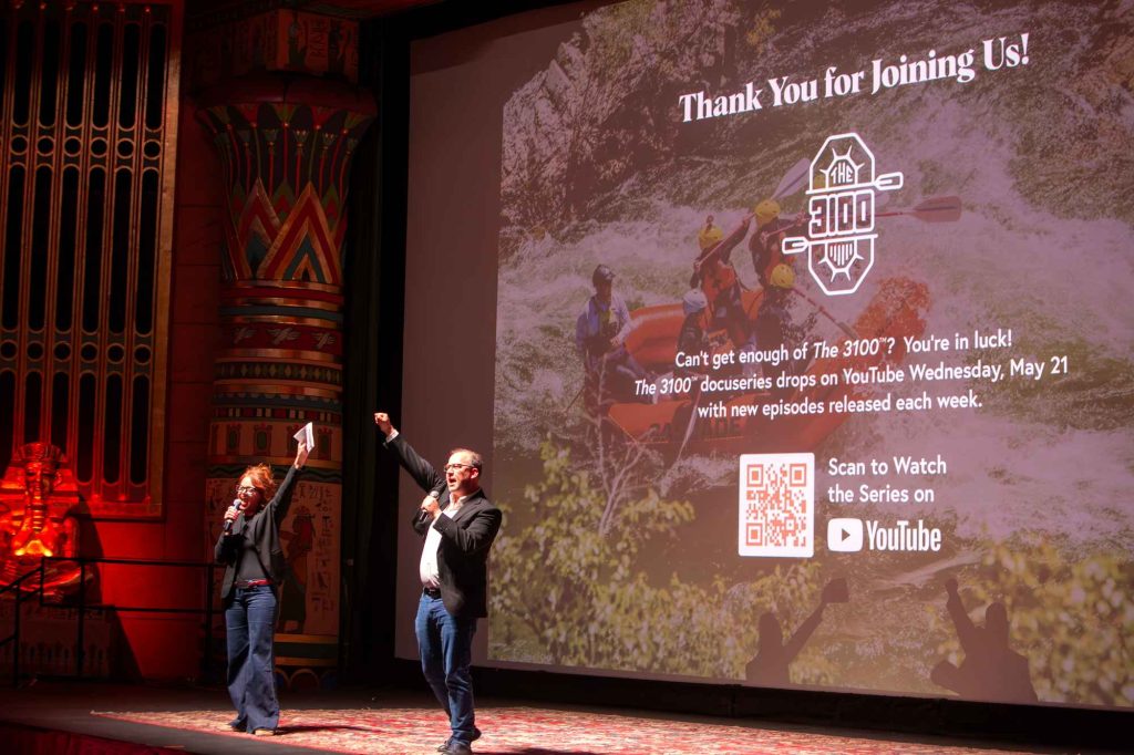 Landing Page Two presenters raise their hands in an air-bump cheers at the Egyptian Theatre, standing in front of a sign thanking the audience for joining.