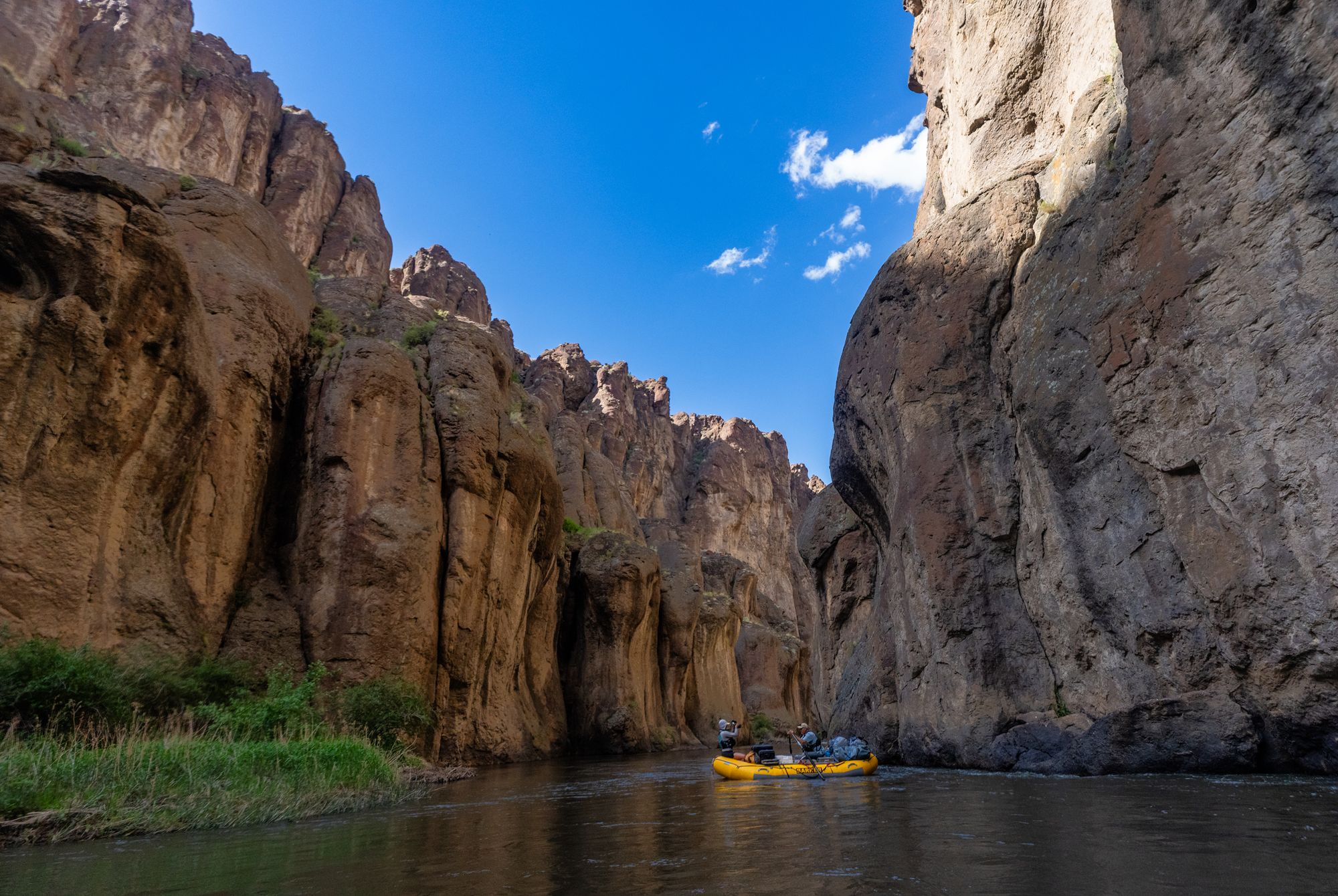 Yellow raft enters a narrow gorge surrounded by towering canyon walls.